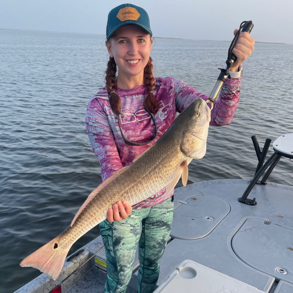girl holding up large redfish on a boat surrounded by water
